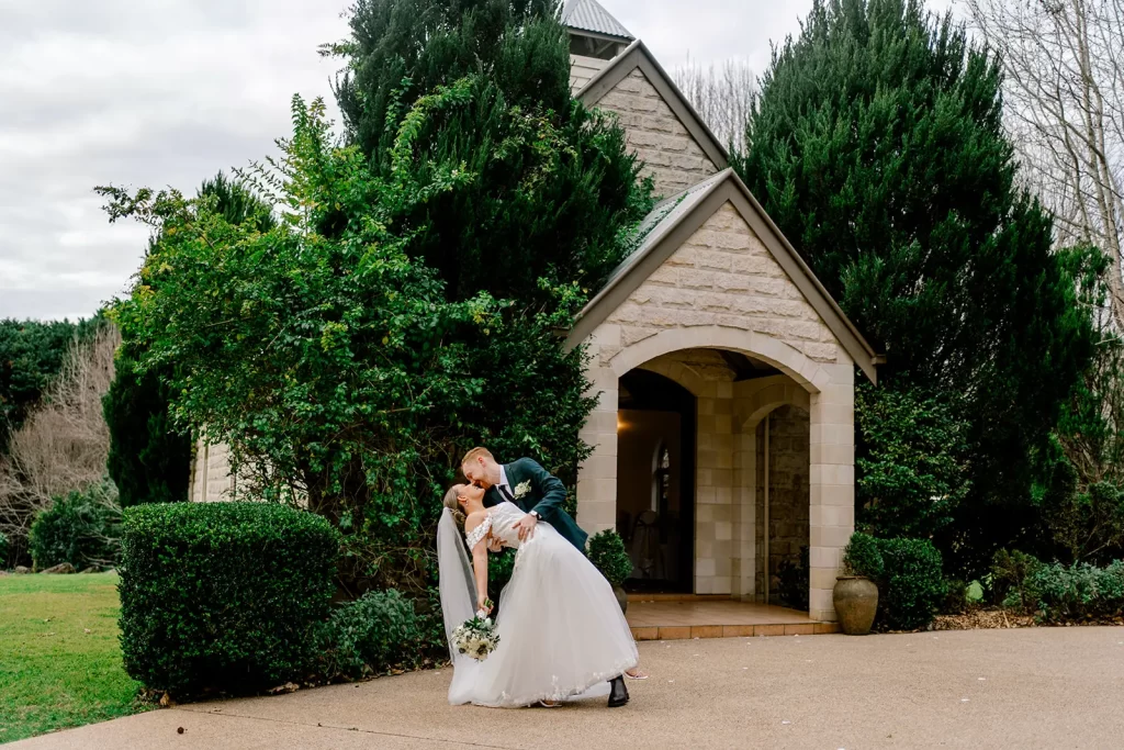 bride and groom kissing in a dip in front of the chapel at cedar creek wedding venue